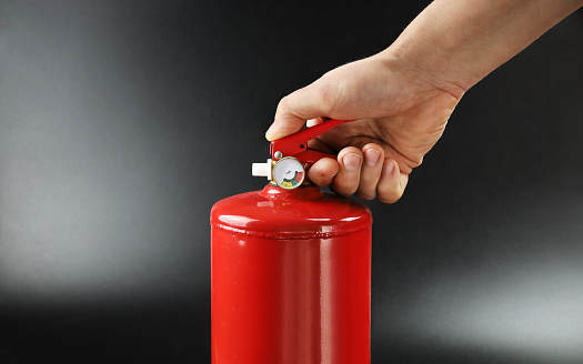 Hand holds fire extinguisher lever with pressure sensor, on black background close-up