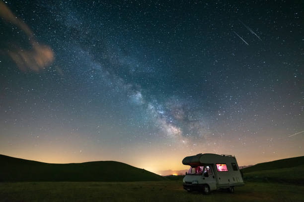 istock Panoramic night sky over Campo Imperatore highlands, Abruzzo, Italy. The Milky Way galaxy arc and stars over illuminated camper van. Camping freedom in unique hills landscape. 1365444433