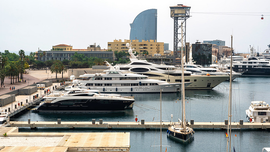 Moored yachts in the Mediterranean sea port, buildings, greenery in Barcelona, Spain