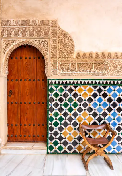 Amazing detail in Alhambra, An old wooden door with an ancient Nasrid's pattern carving on stone wall , Spain - Andalusia