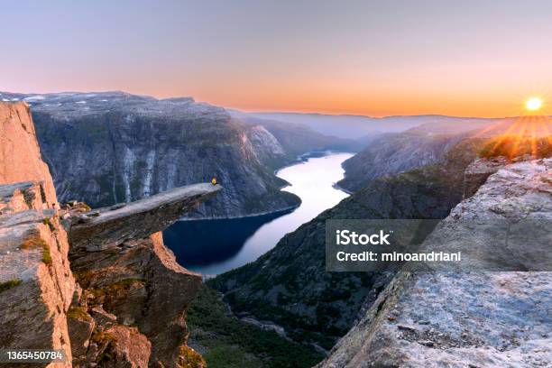 A Man Sits While Throwing His Arms In The Air On The Mountains Cliff Edge Of Trolltunga Throning Over Ringedalsvatnet Watching The Sunset In The Snowy Norwegian Mountains Near Odda Rogaland Norway Stock Photo - Download Image Now
