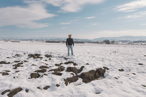 Adult man farmer wearing cowboy hat at his agricultural fields covered with snow