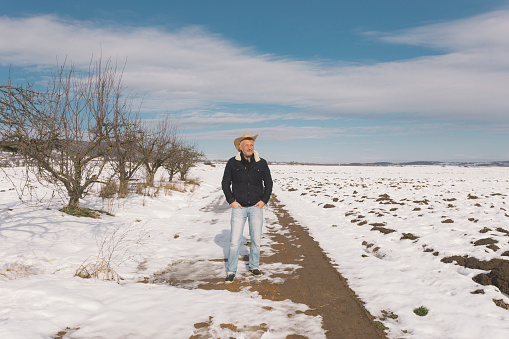 Adult man farmer wearing cowboy hat at his agricultural fields covered with snow