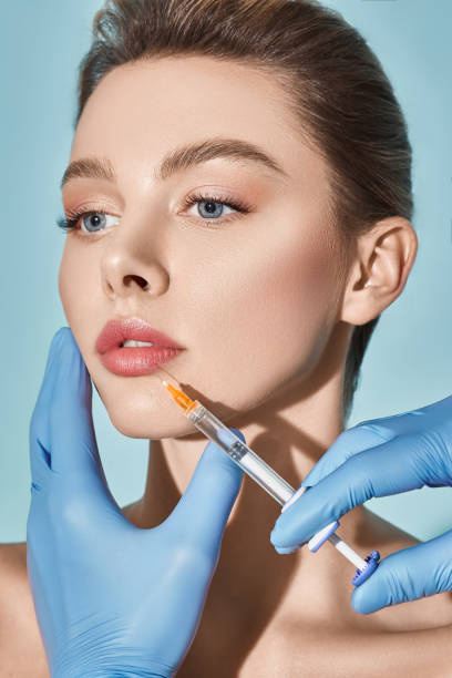 Lip augmentation procedure. Syringe with lips filler near beautiful woman's mouth, injections for increase lips shape stock photo