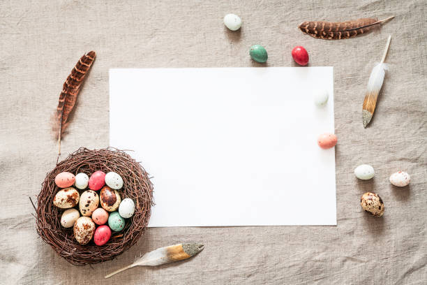 istock Easter background with white paper blank, colored easter eggs, nest and feathers on a beige background 1365455849