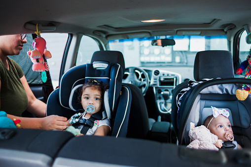 A mother buckles in her two children into their carseats before driving on the road.