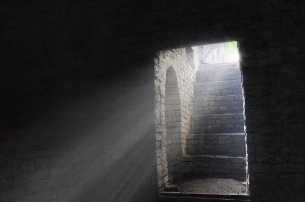 Freedom concept A picture of an old gloomy dungeon lightened by the rays of light through the open door - conceptual image for freedom, imprisonment, liberation etc. dungeon medieval prison prison cell stock pictures, royalty-free photos & images