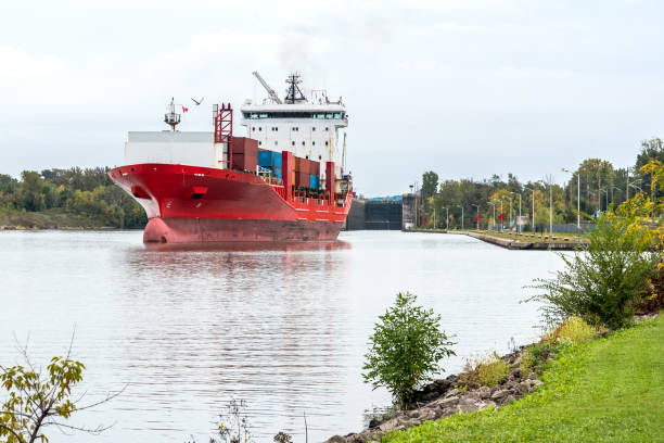 Large container ship sailing up a canal on a cloudy autumn day. A canal lock is visible in background. Welland canal, ON, Canada.