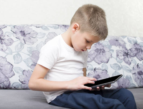 istock The boy sits on the couch and looks at the tablet 1365471110