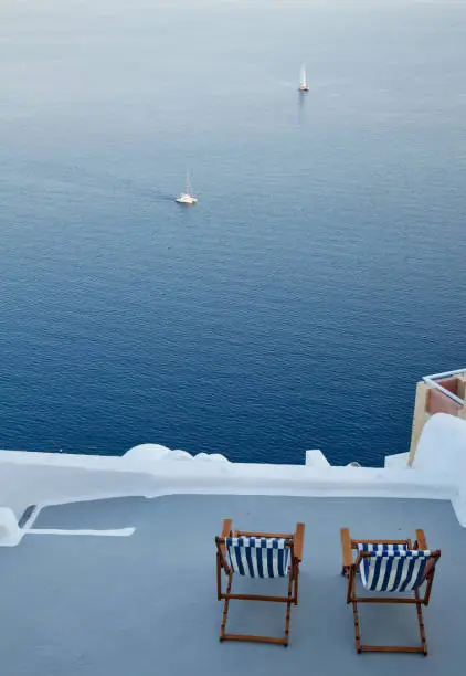 Photo of Two Striped Chairs on Terrace Overlooking the Water and Two Sail