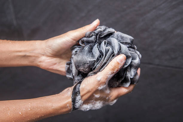 Woman holding black loofah in shower stock photo