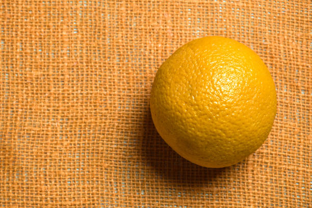 One whole orange on an orange-colored burlap. Close-up. Copy space. Selective focus.