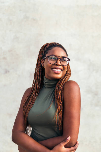 young black woman with glasses smiling happy vertical portrait of a young black woman with glasses smiling happy with a gray concrete wall in the background, concept of youth and racial diversity, copy space for text black woman hair braids stock pictures, royalty-free photos & images