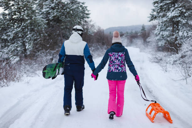istock Beautiful young couple wearing colorful outfits holding hands while walking down a path with their snowboard and sled 1365496091