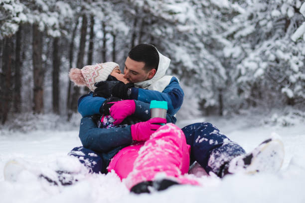 istock Young beautiful and romantic couple sitting down in the snow while drinking hot coffee and having fun 1365496165
