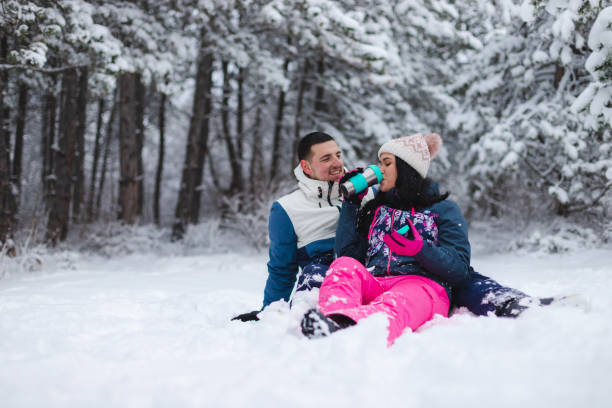 istock Young beautiful and romantic couple sitting down in the snow while drinking hot coffee and having fun 1365496166