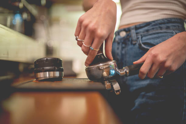 Barista presses ground coffee using tamper. Close-up view on hands with portafilter, small coffee business concept