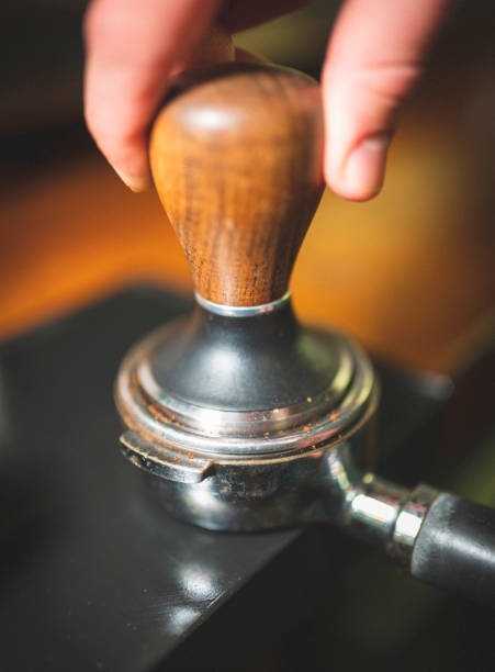 Barista presses ground coffee using tamper. Close-up view on hands with portafilter, small coffee business concept