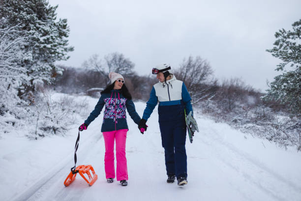 istock Beautiful young couple wearing colorful outfits holding hands while walking down a path with their snowboard and sled 1365496972