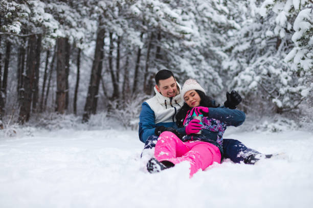 istock Young beautiful and romantic couple sitting down in the snow while drinking hot coffee and having fun 1365497044