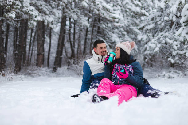 istock Young beautiful and romantic couple sitting down in the snow while drinking hot coffee and having fun 1365497046