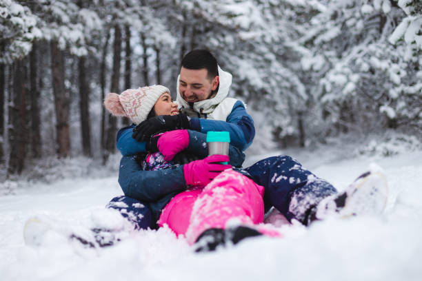 istock Young beautiful and romantic couple sitting down in the snow while drinking hot coffee and having fun 1365497048