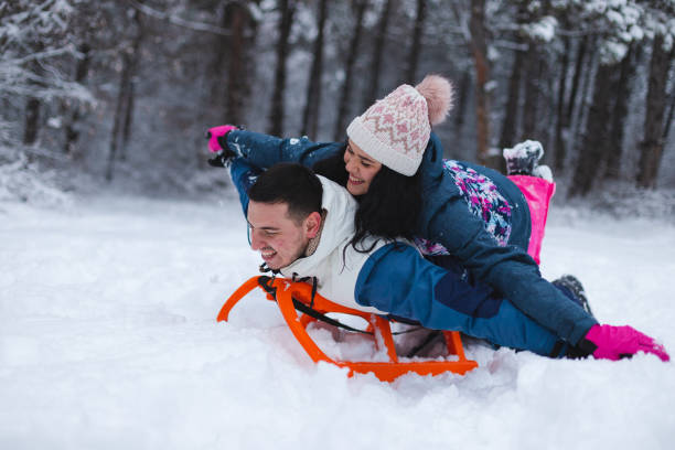istock Young beautiful and romantic couple having fun in the snow while laying on a sled 1365497070