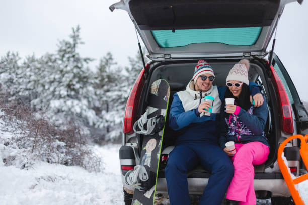 스키/스노우보드 세션을 준비하는 동안 가족 용 자동차 트렁크에 앉아 뜨거운 커피를 마시는 젊고 낭만적 인 미소 짓는 커플 - romance skiing ski resort couple 뉴스 사진 이미지
