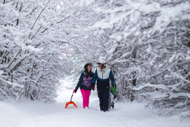 istock Young beautiful and romantic couple pulling their sled and holding their snowboard while walking through a snowy environment 1365497157
