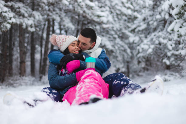 istock Young beautiful and romantic couple sitting down in the snow while drinking hot coffee and having fun 1365497688