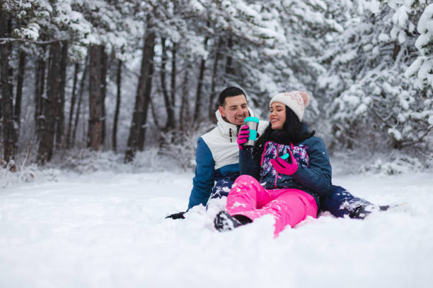 istock Young beautiful and romantic couple sitting down in the snow while drinking hot coffee and having fun 1365497692
