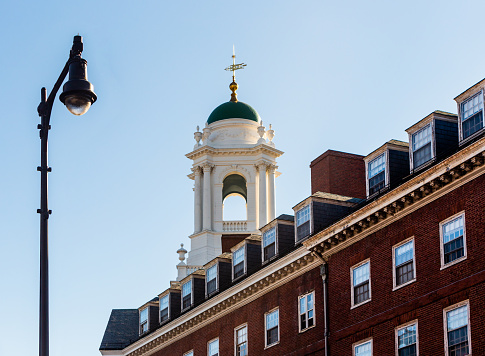 Cambridge, Massachusetts, USA - January 16, 2022: Eliot House tower cupola with green dome. Eliot House (c. 1931) is one of the twelve undergraduate residential Houses at Harvard University. Low angle view from street, including street light and portion of building.