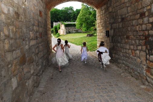Wedding day.young bridesmaids running under a medieval castle postern of the 12th century.