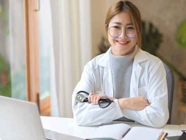 女性医師や医師は、彼女のオフィスの机に交差して腕を持って座っていました。 - physical therapy arms crossed smiling women ストックフォトと画像