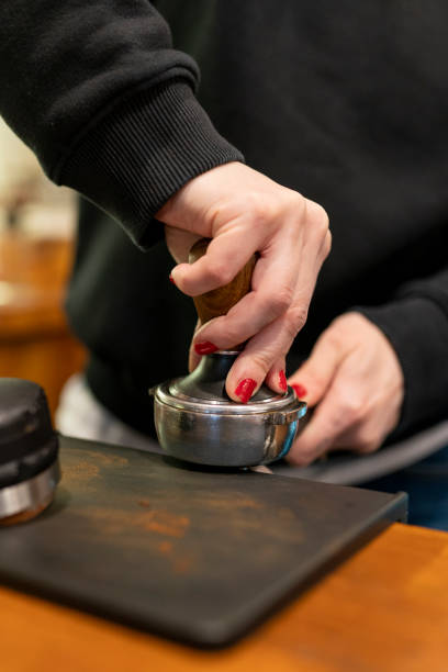 Barista presses ground coffee using tamper. Close-up view on hands with portafilter, small coffee business concept