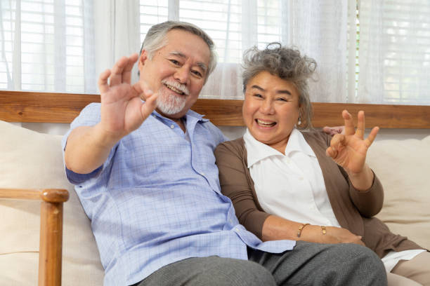 自宅のリビングルームでokサインをやってポジティブに微笑む幸せな高齢のアジアのカップル - senior adult retirement mature adult couple ストックフォトと画像