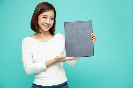 Happy Asian woman holding policy insurance book on hand isolated on green background