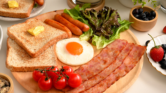 Close-up image, A plate of a healthy breakfast set with sunny egg, grilled bacons and sausages, toasts and fresh vegetables.