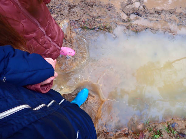 istock Spring puddle.puddle walk. feets in blue and pink rubber boots in spring muddy water.steps in the water. rubber boots walks through the puddles.Spring mud and puddles. 1365519811
