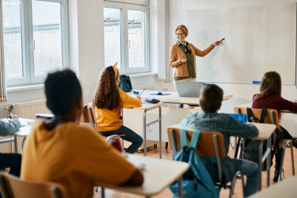 istock Happy math teacher giving lecture on whiteboard to elementary students in the classroom. 1365527760