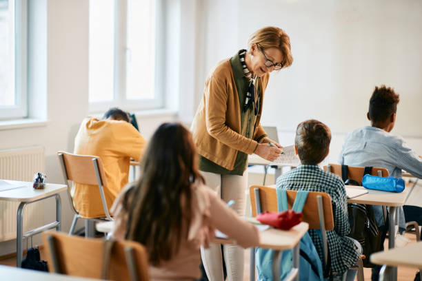 istock Mature teacher assisting her student on a class at elementary school. 1365527801