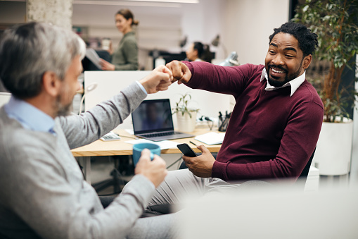 Male entrepreneurs fist bumping while greeting in the office. Focus is on African American businessman.