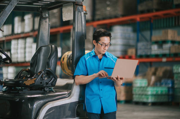 istock Asian Chinese Foreperson using laptop checking inventory at warehouse beside forklift 1365528990