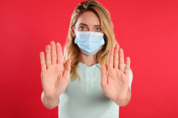 istock Woman in protective face mask showing stop gesture on red background, focus on hands. Prevent spreading of coronavirus 1365530198