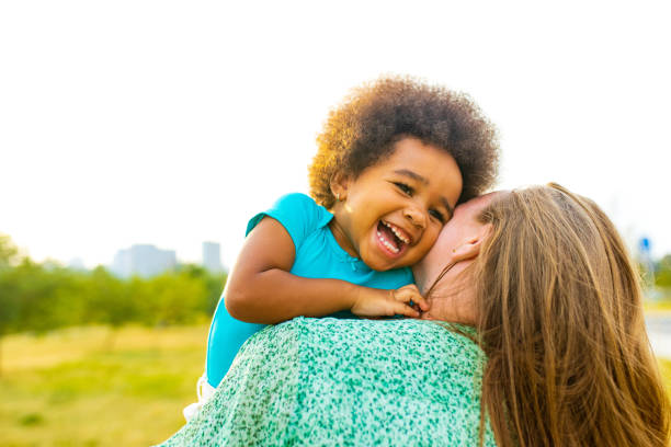 Mother is hugging her daughter at home. Bright light is coming through the window in the background.