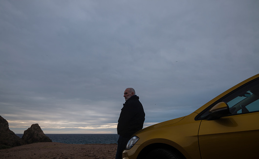Adult man standing against car looking at view during sunset. Almeria, Spain