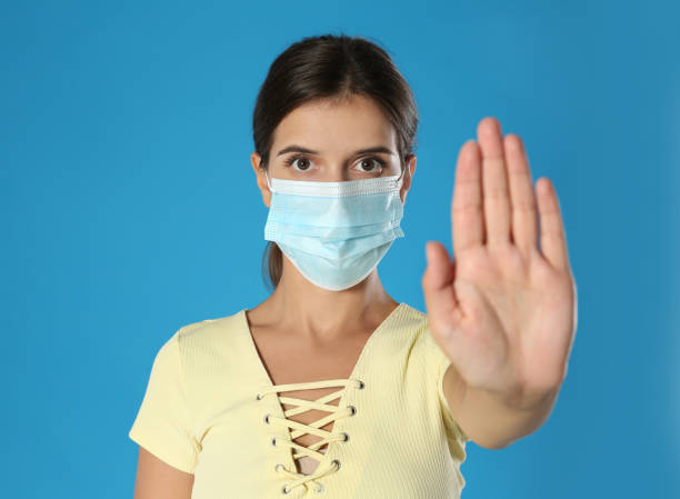 istock Woman in protective mask showing stop gesture on blue background, space for text. Prevent spreading of coronavirus 1365532952