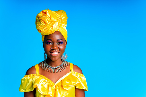 African woman with yellow silk turban and silver earrings and nose piercing in blue studio background.