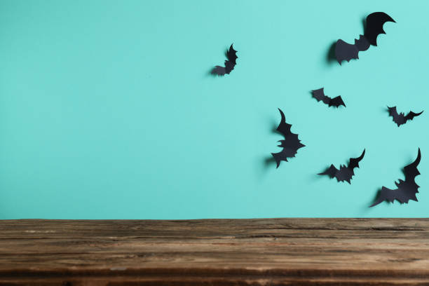 istock Empty wooden table near light blue wall decorated with paper bats, space for text. Halloween celebration 1365533597