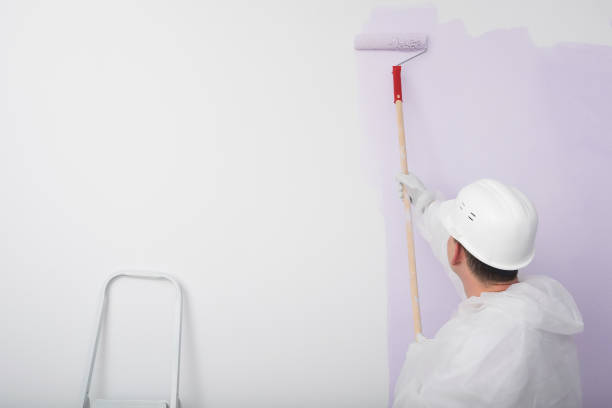 istock a worker in a hard hat paints a white wall with a roller in lilac color 1365534185